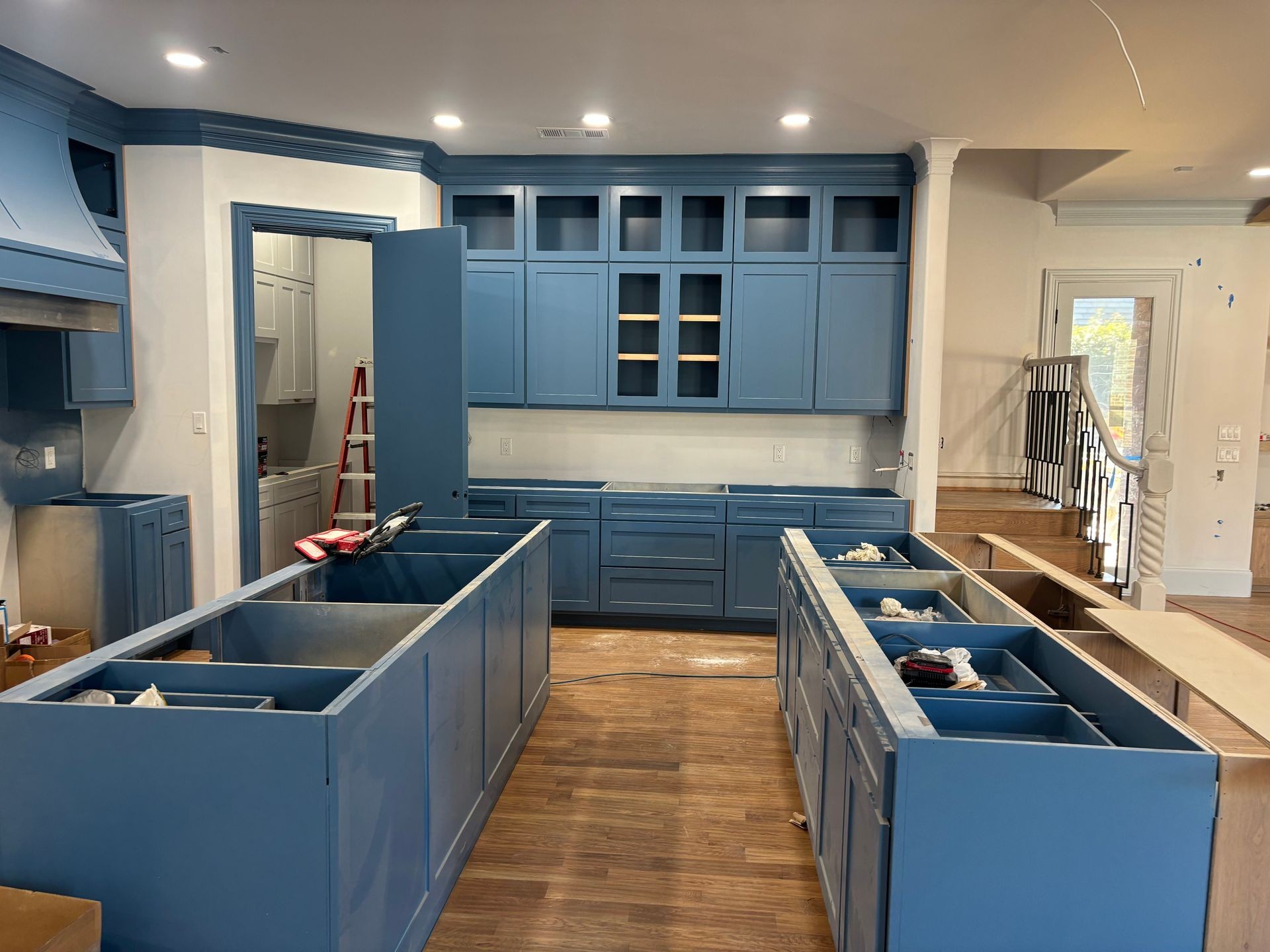 Modern kitchen under construction with blue cabinets and wooden flooring.