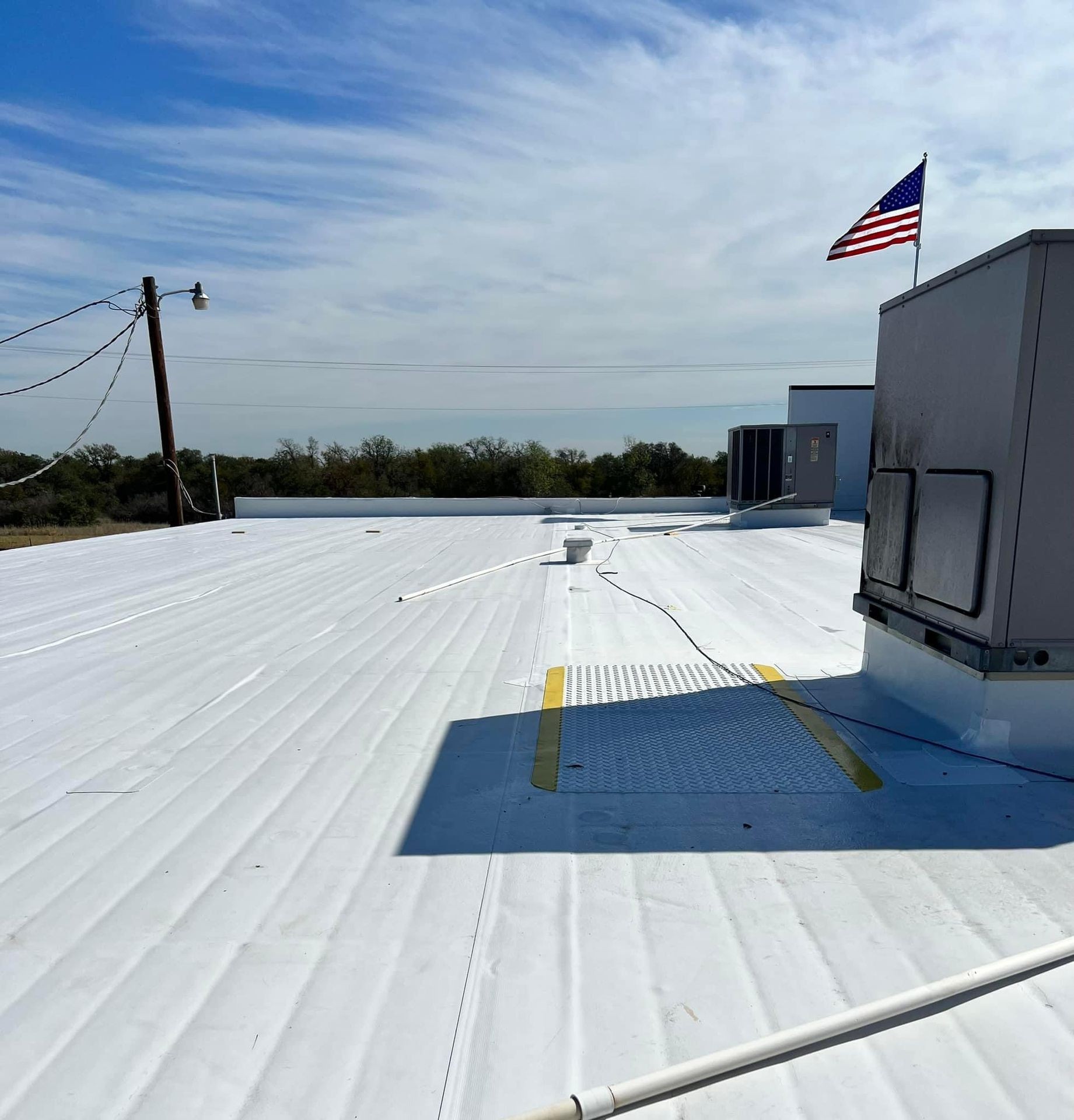 Flat white rooftop with an American flag and air conditioning units under a blue sky.